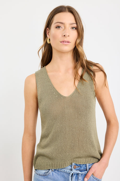 Woman wearing a sleeveless khaki knit top with a V neckline and relaxed fit, styled with light blue jeans.