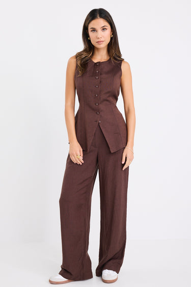Woman wearing wide-leg chocolate brown trousers with a mid-rise waist.