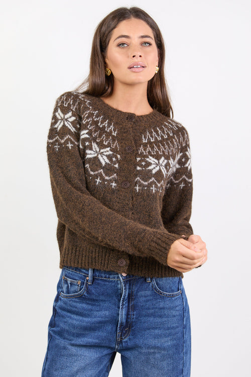 Woman wearing a brown knitted cardigan with white patterns on a plain background