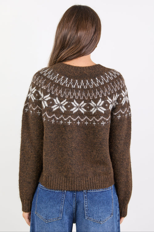 Person wearing a brown sweater with a white pattern, standing against a white background
