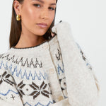 A woman wearing a cosy cream-colored cardigan with a Fair Isle pattern in shades of brown and blue, paired with high-waisted, relaxed-fit blue jeans.