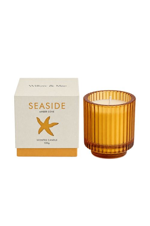 A Seaside Amber Cove scented candle by Willow & Moss, shown with its cream-colored packaging box and a ribbed amber glass jar candle on a plain white background.