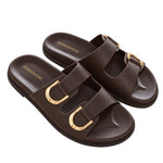 A pair of dark brown double-strap slide sandals with prominent gold-tone metal buckles, shown on a plain white background.