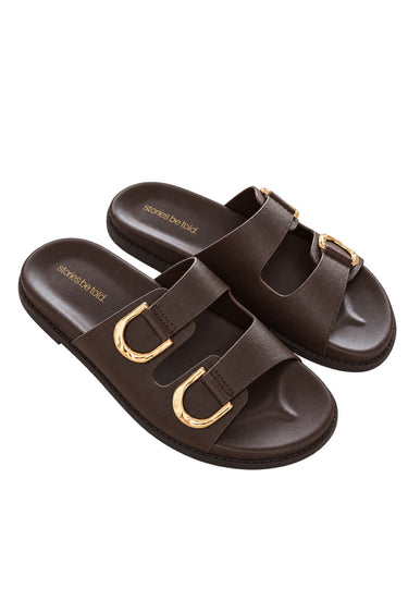 A pair of dark brown double-strap slide sandals with prominent gold-tone metal buckles, shown on a plain white background.