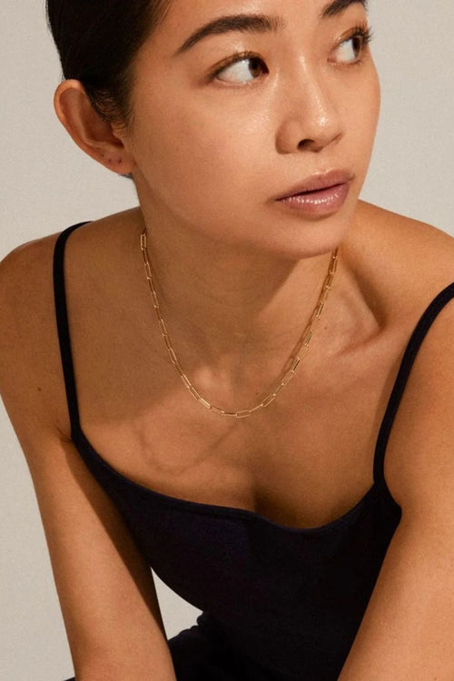 Woman wearing a gold necklace against a neutral background