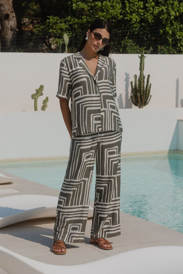 Woman wearing a short-sleeve shirt with an abstract olive and cream geometric print and button front,