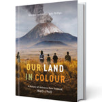 A hardcover book titled "Our Land in Colour" shown at a slight angle against a plain white background. The cover features a photograph of a volcanic landscape with silhouetted figures in the foreground and the subtitle "A History of Aotearoa New Zealand 1860-1960.