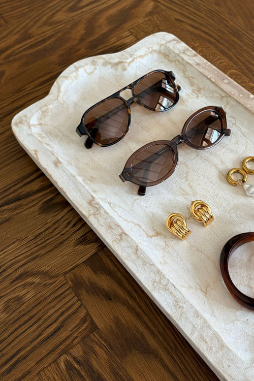 Sunglasses and earrings on a marble tray with a wooden background
