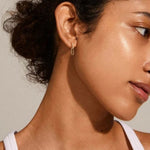 Close-up of a woman wearing a gold hoop earring with a neutral background