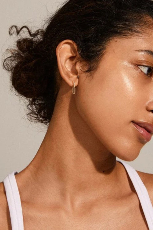 Close-up of a woman wearing a gold hoop earring with a neutral background