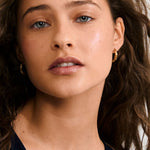 Close-up of a woman with wavy hair wearing gold hoop earrings.