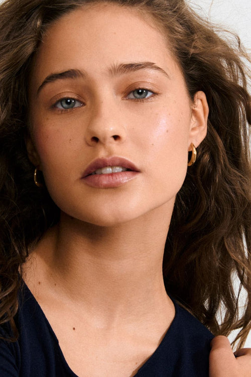 Close-up of a woman with wavy hair wearing gold hoop earrings.