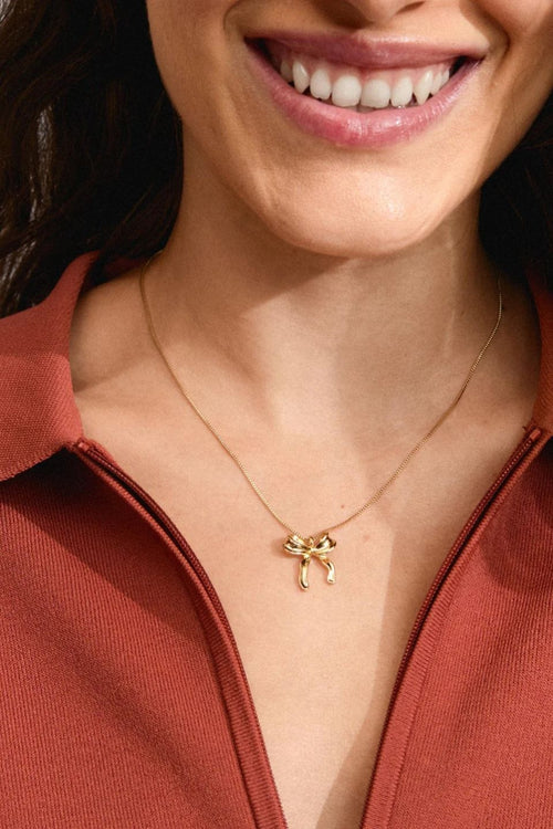 Close-up of a woman wearing a gold necklace with a bow pendant.