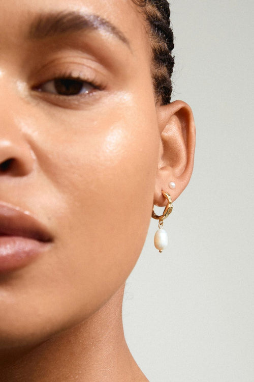 Close-up of a person wearing gold hoop earrings with pearl accents.
