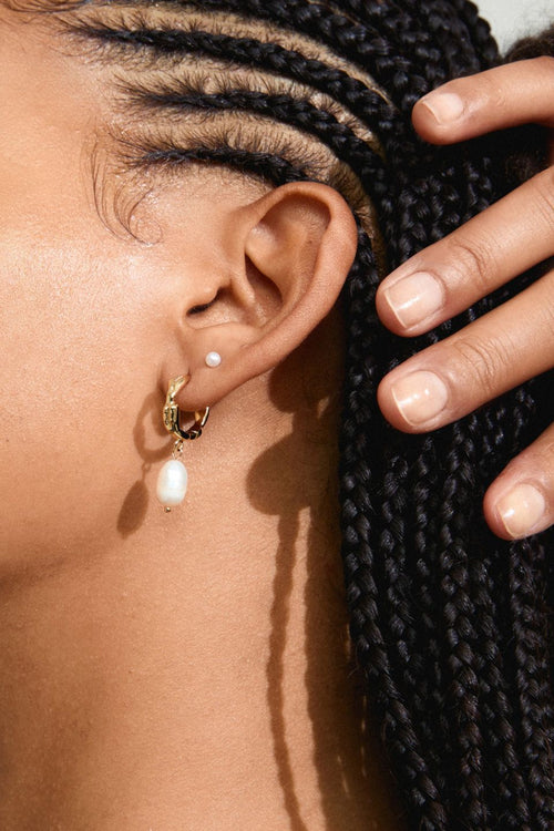 Close-up of an ear with earrings and a hand adjusting hair.