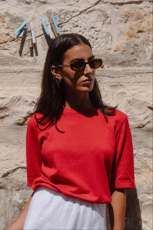 model wears a red knit t-shirt with white linen skirt