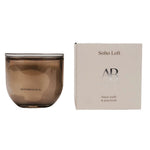 A brown translucent glass jar candle next to its cream-colored packaging box, featuring the brand name 'AB' and scent name 'Soho Loft'.