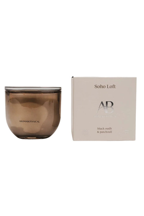 A brown translucent glass jar candle next to its cream-colored packaging box, featuring the brand name 'AB' and scent name 'Soho Loft'.
