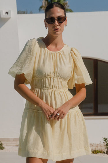 Woman wearing a short butter-yellow mini dress with puff sleeves