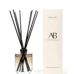 A reed diffuser bottle with black reeds next to its cream-colored packaging box, set against a plain white background.