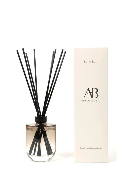 A reed diffuser bottle with black reeds next to its cream-colored packaging box, set against a plain white background.