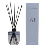 A reed diffuser bottle with black reeds next to its light blue packaging box. The box is branded 'The Powder Room' and 'AB All Purpose Room'.