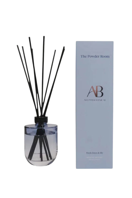 A reed diffuser bottle with black reeds next to its light blue packaging box. The box is branded 'The Powder Room' and 'AB All Purpose Room'.