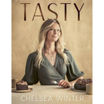 Book cover of 'TASTY' by Chelsea Winter, featuring a portrait of the author seated at a table with cakes and coffee against a warm beige background.