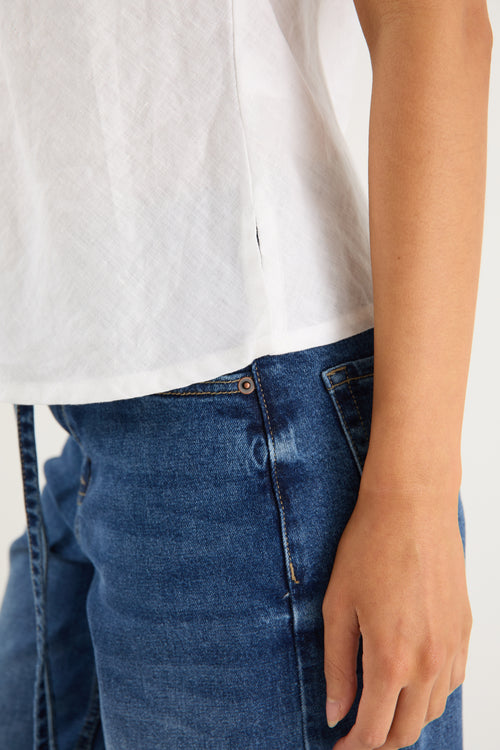 Model wears a white linen tank top with dark denim jeans