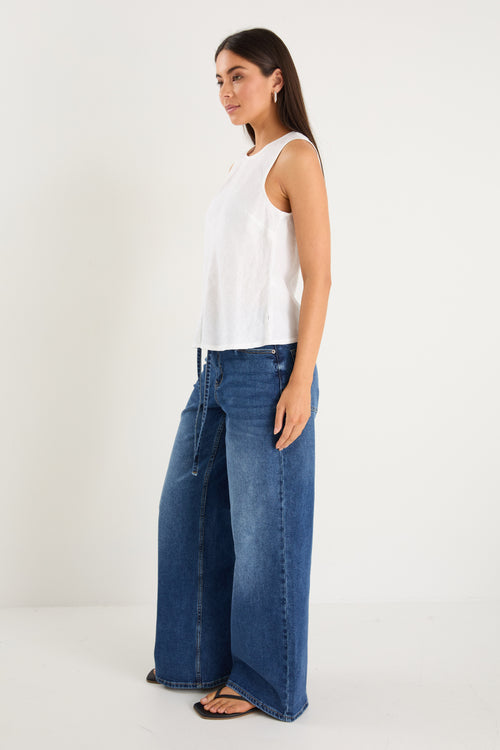 Model wears a white linen tank top with dark denim jeans