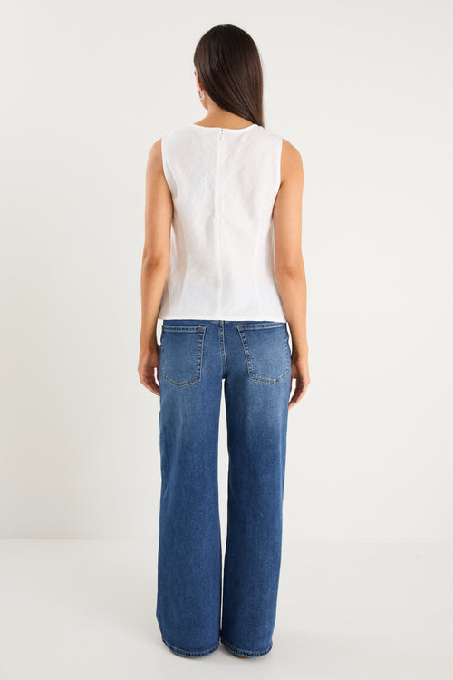 Model wears a white linen tank top with dark denim jeans
