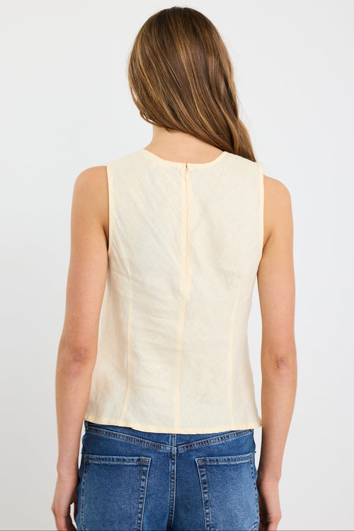 Woman wearing a sleeveless butter-yellow linen shell top with a round neckline and relaxed bias cut, styled with deep blue jeans.