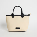 Natural canvas mini handbag with black PU trim, small knotted top handles and a long detachable shoulder strap, photographed against a plain background