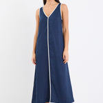 A sleeveless navy dress with ecru contrast piping down the front, featuring side pockets and a relaxed fit. Made from 100% linen for a breathable, comfortable feel.