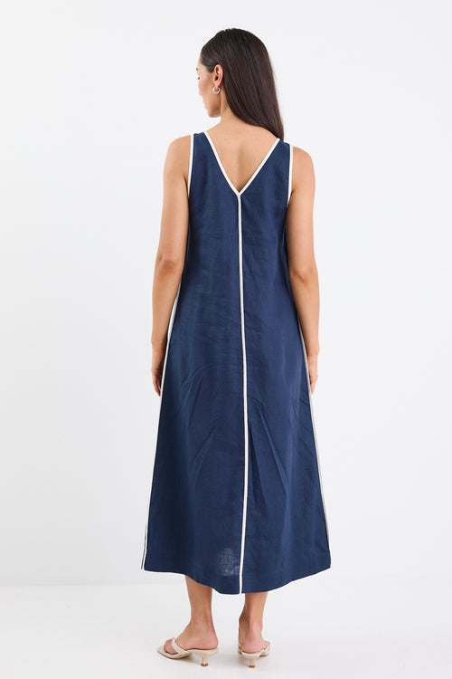 A sleeveless navy dress with ecru contrast piping down the front, featuring side pockets and a relaxed fit. Made from 100% linen for a breathable, comfortable feel.