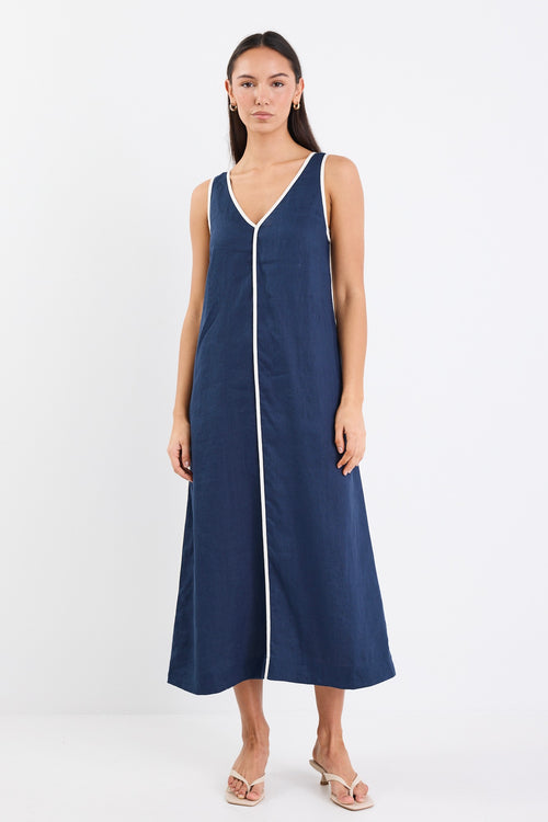 A sleeveless navy dress with ecru contrast piping down the front, featuring side pockets and a relaxed fit. Made from 100% linen for a breathable, comfortable feel.