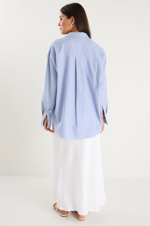 Model wears a blue linen shirt with a white maxi skirt