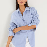 Model wears a blue linen shirt with a white maxi skirt