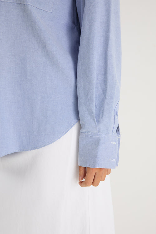 Model wears a blue linen shirt with a white maxi skirt