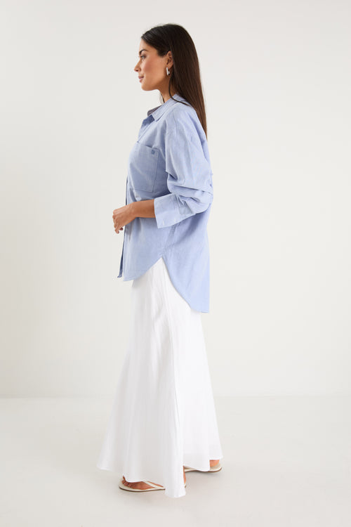 Model wears a blue linen shirt with a white maxi skirt