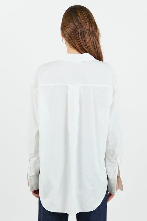 A woman wearing a classic white button-down shirt with a pocket on the left chest, paired with dark indigo wide-leg jeans. She is standing with one hand in her pocket, showcasing a relaxed and casual look.