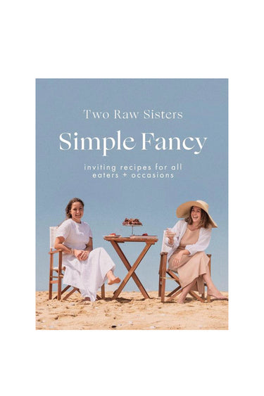 Book cover of 'Simple Fancy' by Two Raw Sisters with two women sitting at a table on a beach.