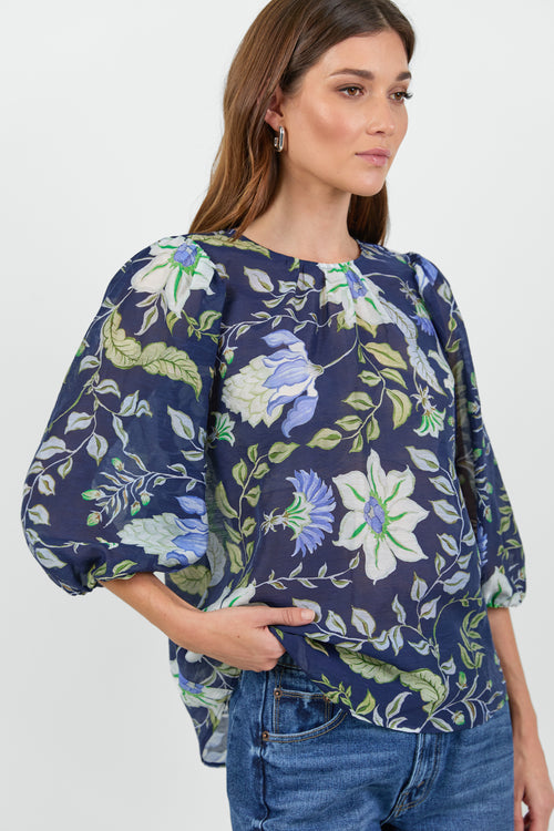 Close up of a woman wearing a floral blouse and blue jeans on a white background.