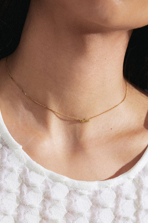 model wearing gold necklace with a pendant reading 