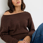 Woman wearing a brown sweater and blue jeans against a white background