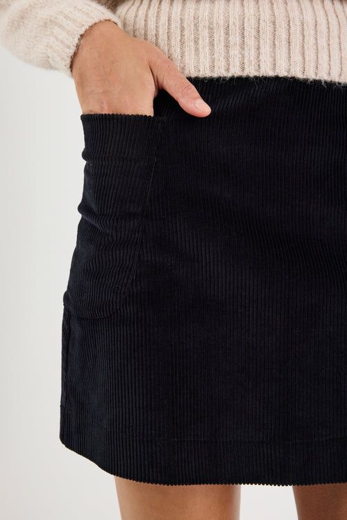 Black corduroy skirt worn with a beige sweater on a light background