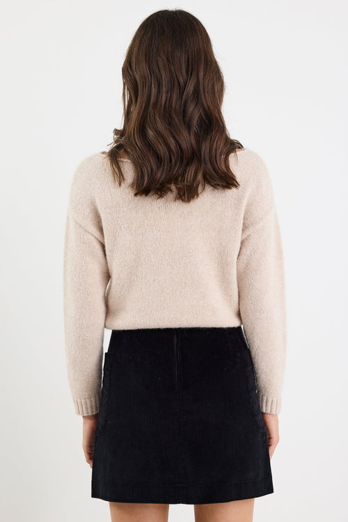 Person wearing a beige sweater and black skirt on a white background