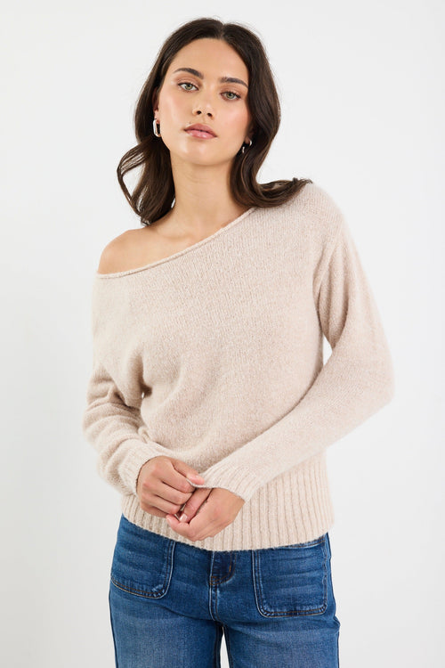 Woman wearing a beige off-shoulder sweater and blue jeans on a white background