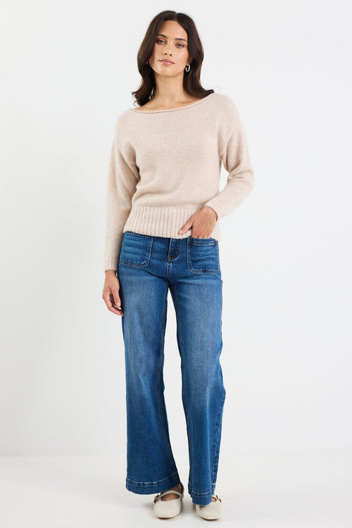 Woman wearing a beige sweater and blue jeans on a white background