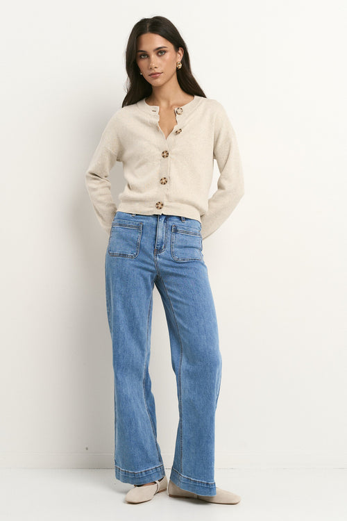 Woman wearing a beige cardigan and blue jeans on a white background